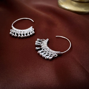 Detailed view of silver metallic C-shaped earrings with teardrop tassels on silk fabric