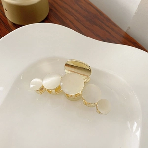 Macro detail of golden metal hair claw clip with opal-like stone inlays on ceramic plate