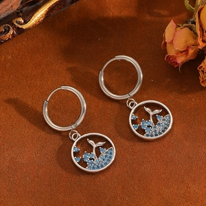Detailed close-up of silver hollow whale tail hoop earrings with blue rhinestones