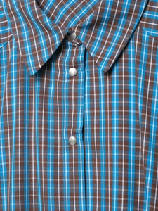 Détail de la robe à carreaux bleus et bruns avec boutons-pression en métal argenté