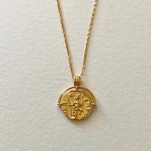 Macro detail of a vintage gold portrait coin pendant with textured relief on a thin chain