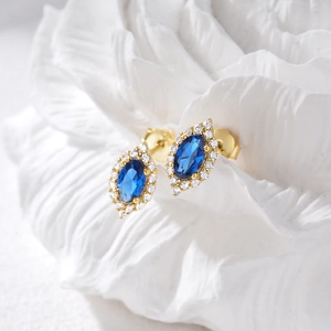 Detailed shot of golden marquise blue stone earrings with diamond accents on white relief