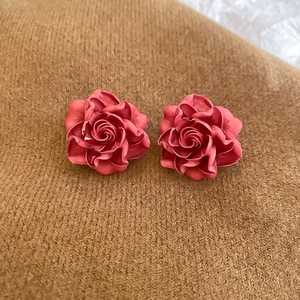 Detailed macro shot of vintage red resin rose earrings on a soft textured brown fabric