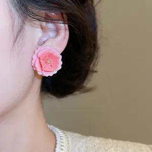 Élégantes boucles d'oreilles fleurs en résine rose portées par un mannequin en lumière