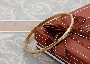 Dettaglio del bracciale rigido dorato con cristalli scintillanti su scatola regalo