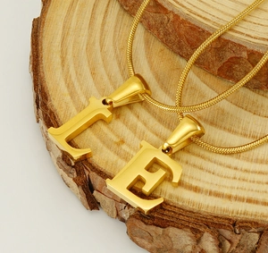 Macro view of gold snake chain with L and E letter pendants on a natural wood surface