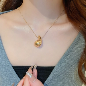 Close-up of golden teardrop pendant on a fine snake chain necklace worn by a model