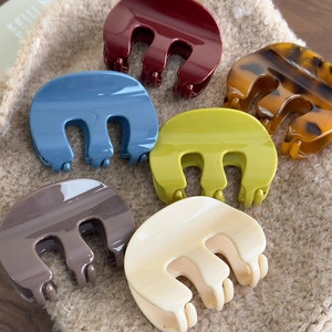 Group of six colorful M-shaped acrylic hair claws on a beige plush background