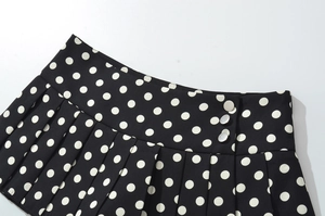 Détail d'une jupe plissée noire à pois avec des boutons argentés sur le côté de la taille