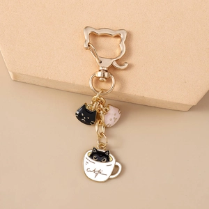 Detail of a golden cat-shaped keychain featuring enamel cat charms and a coffee cup pendant