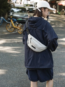 Minimalist beige canvas chest bag shown on a model in a casual outdoor street setting