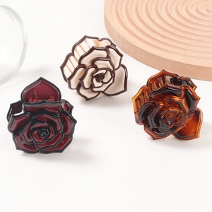 Elegant rose-shaped hair claw clips in red, beige, and amber colors on a clean white surface