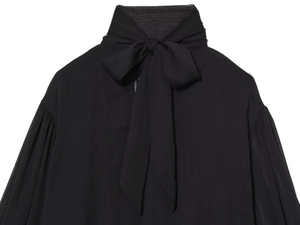 Detail van de hoge kraag met een grote strik en geplooide manchetten op de blouse