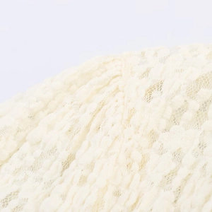 Close-up of cream lace fabric texture with bow detail on a stylish short jumpsuit