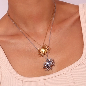Close-up of gold and silver crab pendants on necklaces worn by a model in soft pink lighting