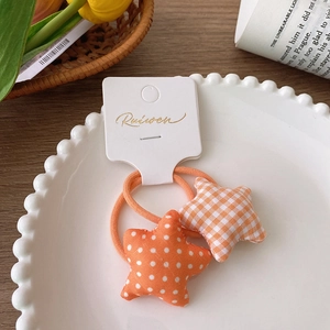 Detail of star-shaped fabric hair ties with orange polka dots and check patterns on a tray