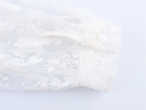 Detailed view of white mesh sleeve with flocked floral patterns and button closure
