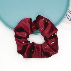 Detailed close-up of a burgundy velvet scrunchie featuring gold foil star patterns