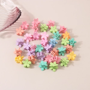 Mini macaron flower hair clips in various colors spread on a cream background