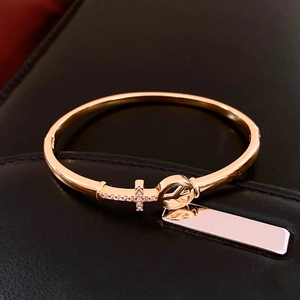 Detail of 18K gold plated arrow cross bangle with peace symbol and dangling metal tag