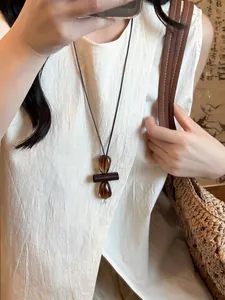 Macro detail of geometric wood and amber resin pendant on a long minimalist cord necklace