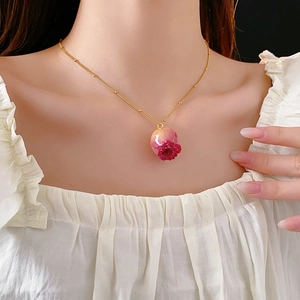 Detail of a gold necklace featuring a rose flower pendant in a transparent resin orb