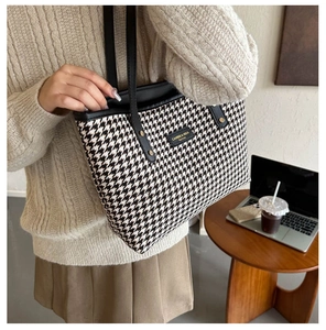 Detail of houndstooth tote bag with leather trim on a wooden table in office setting