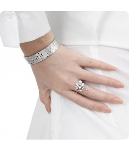 Detail of silver floral ring and textured cuff bracelet worn on model with white shirt