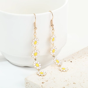 Elegant gold drop earrings with white daisy flower enamel charms on a white cup