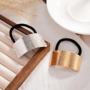 Detailed view of silver and gold textured metal ponytail holders on a wooden tray