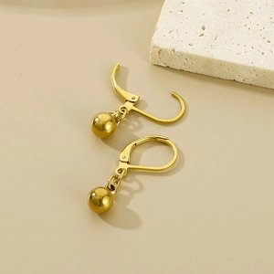 Detail view of golden stainless steel ball drop earrings with leverback closure on beige stone