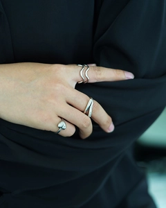 Three minimalist silver rings featuring wave shapes and heart patterns on hands