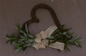 Detail view of heart-shaped vine wreath with olive branches and rustic burlap bow