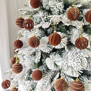 Détails de boules de Noël en velours marron avec motifs dorés sur branches enneigées
