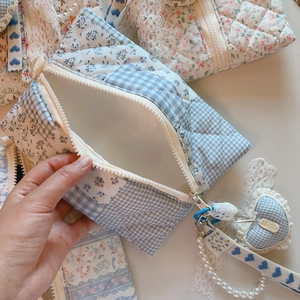 Detail of blue floral quilted cosmetic bag featuring lace trim and a heart pendant