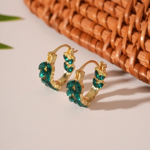 Close-up of gold ear hoops with emerald marquis rhinestones on woven basket decor