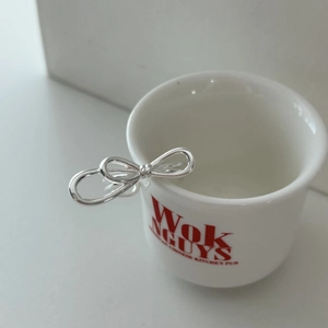 Polished 925 sterling silver bow knot open ring displayed on a white ceramic cup edge