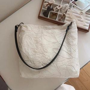 Close-up of beige cotton tote bag featuring leaf embroidery and black leather strap
