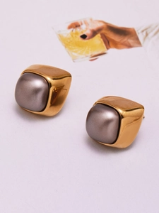 Detailed close-up of geometric gold stud earrings with grey pearls on a textured background