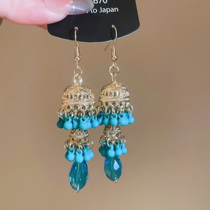 Detailed view of gold flower earrings with turquoise beads and blue teardrop pendant