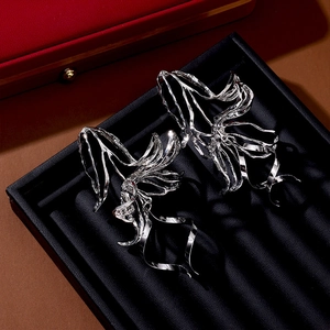 Macro shot of silver metallic flower earrings with abstract flowing petals on a black tray
