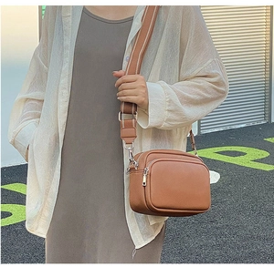 Brown crossbody camera bag with wide striped strap and dual zippers shown in lifestyle view