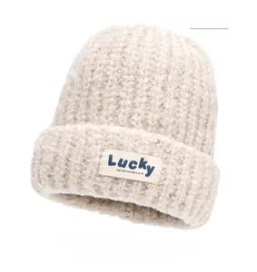Close-up of off-yellow knitted beanie with Lucky patch and thick ribbed texture