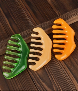 Three 8-tooth meridian massage combs in green, yellow and orange colors on wood surface