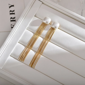 Elegant long fringe earrings with white square pearls and gold chain tassels on jewelry box