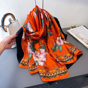 Orange floral silk scarf with bohemian patterns displayed on a minimalist hanger