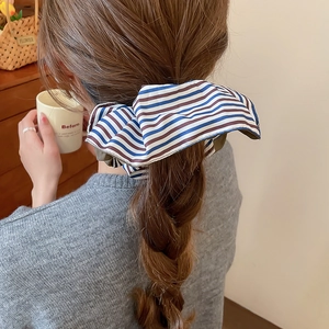 Gros plan d'un chouchou en tissu rayé bleu, blanc et marron sur une queue de cheval