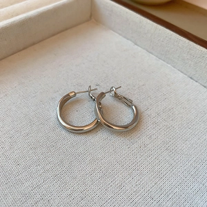 Close-up of polished silver hoop earrings on a textured fabric tray with soft lighting