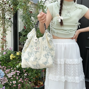 Detailed macro view of the cream plush tote bag featuring blue butterfly prints and woven handles