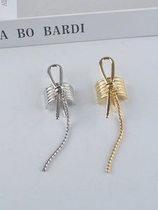 Detail of metal bow ear cuffs with long tassels in gold and silver finish